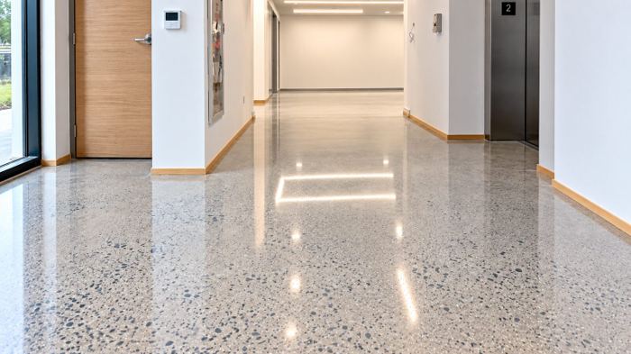 Elevator lobby and corridor finished in polished concrete, the aggregate-speckled slab running past the elevator doors into the corridor beyond