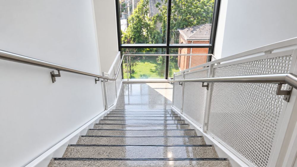 Polished concrete stair run descending toward a full-height window, aggregate visible in the treads and landing below
